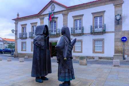 MIRANDA DO DOURO, PORTUGAL - DEC 25, 2017: Bronze statues of Man wearing an Honor Cape and woman with traditional winter clothes (by Jose Antonio Nobre), with the town hall, Miranda do Douro, Portugalのeditorial素材