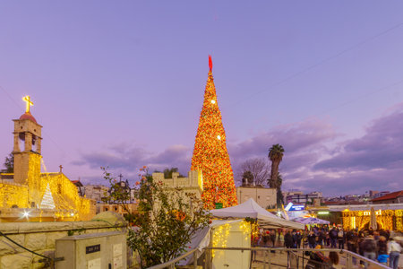 Nazareth, Israel - December 24, 2021: Evening scene of the church square (near Mary well), with the Greek Orthodox Church of the Annunciation, Christmas tree, and crowd, in Nazareth, Israelのeditorial素材