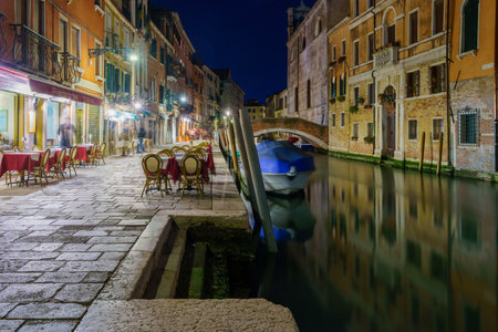 Venice, Italy - February 27, 2022: Night view of canal, boat, bridge, and restaurants, in Venice, Veneto, Italyのeditorial素材