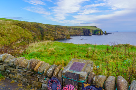 Windwick, UK - October 05, 2022: View of cliffs along the coastline, with memorial plate, Ossi Taking point, and Windwick Bay. Island of South Ronaldsay, Orkney Islands, Scotland, UKのeditorial素材