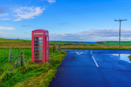 View of a red phone box, in a landscape of fields with road, in the Orkney Islands, Scotland, UKの写真素材