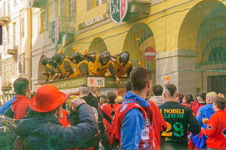 Ivrea, Italy - February 19, 2023: Groups in traditional dressings, and crowd with red hats, take part in the Battle of the Oranges, part of the historical carnival of Ivrea, Piedmont, Northern Italyのeditorial素材