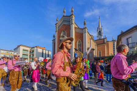 Cantu, Italy - February 25, 2023: Carnival parade, musician band, crowd and the Church of Saints Michael and Blaise, in Cantu, Lombardy, Northern Italyのeditorial素材