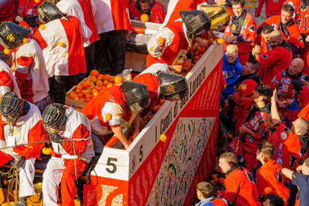Ivrea, Italy - February 19, 2023: Groups in traditional dressings, and crowd with red hats, take part in the Battle of the Oranges, part of the historical carnival of Ivrea, Piedmont, Northern Italyのeditorial素材