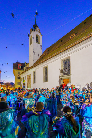 Lucerne, Switzerland - February 20, 2023: Band of musicians in costumes and crowd, near the St. Peter Chapel, at sunrise, part of the Fasnacht Carnival, in Lucerne (Luzern), Switzerlandのeditorial素材