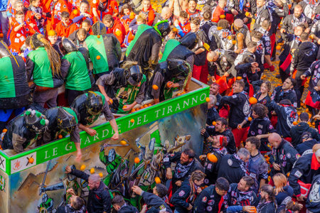 Ivrea, Italy - February 19, 2023: Groups in traditional dressings, and crowd with red hats, take part in the Battle of the Oranges, part of the historical carnival of Ivrea, Piedmont, Northern Italyのeditorial素材