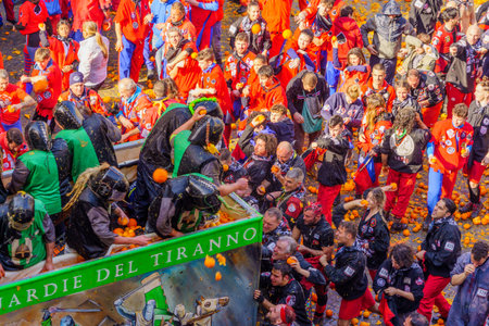 Ivrea, Italy - February 19, 2023: Groups in traditional dressings, and crowd with red hats, take part in the Battle of the Oranges, part of the historical carnival of Ivrea, Piedmont, Northern Italyのeditorial素材