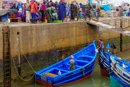 Essaouira, Morocco - April 07, 2023: Sunrise scene of the fishing port, with fishermen delivering baskets of sardines (long exposure), in Essaouira (Mogador), Moroccoのeditorial素材