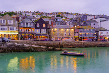 St Ives, UK - October 14, 2022: Sunset view of the harbor, with various businesses, in St Ives,...