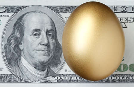 A golden egg with the US one hundred dollar bill in the background  (shallow depth of field).の写真素材