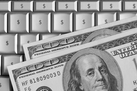 US hundred dollar bills on top of a laptop. Keyboard characters replaced with dollar signs. の写真素材