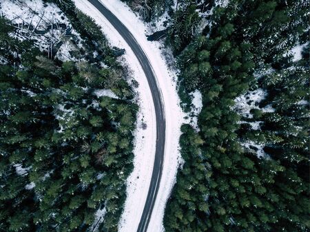 Aerial Drone Photography of a Road in Winter, Between Woods with a Snow on a cloudy Winter Dayの写真素材