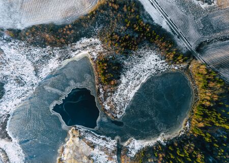 Aerial Drone Photograph of a Partly Frozen Lake Surrounded with Beautiful Winter Colors of the Fields and Forestの写真素材