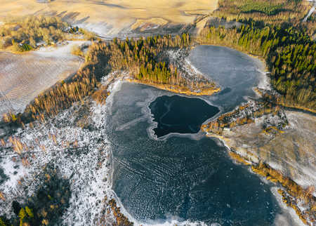 Aerial Drone Photograph of a Partly Frozen Lake Surrounded with Beautiful Winter Colors of the Fields and Forestの写真素材