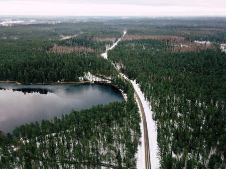 Aerial Drone Photography of a Road in Winter, Between Woods with a Snow on a Cloudy Dayの写真素材