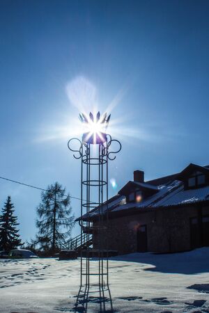 Calm, Cold and Sunny Winter Day with Sun Star Shining into Camera Through Metal Crown Ornament with House on a Backgroundの写真素材