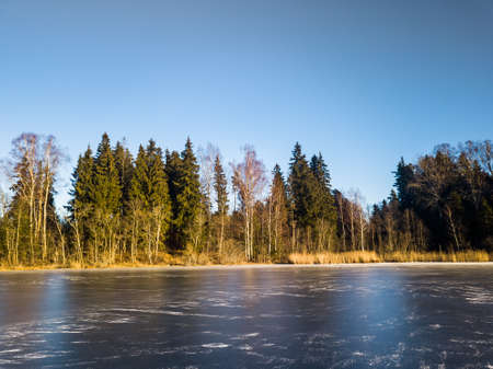 Beautiful Photo of a Frozen Lake in Sunny Autumn Day in an October, with a Sun Shining at Tree line on the coast of Lakeの写真素材
