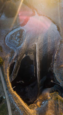 Aerial Drone Photograph of a Partly Frozen Lake Surrounded with Beautiful Winter Colors of the Fields and Forest - Sun Flareの写真素材