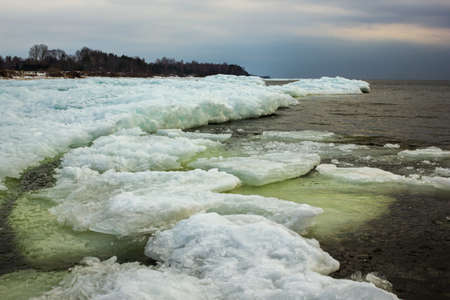 Baltic Sea Beach with Ice Floating in a Water, through Natural Frame of two Snow Piles on a Sunny...