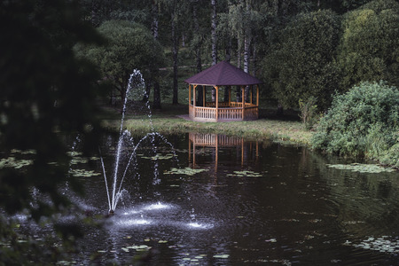 Moody, Dark Photo of the Wooden Summer Garden House in a Park, Between Woods with the Park Fountain...