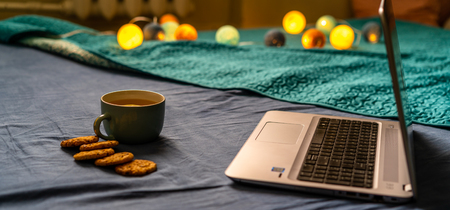 Tea with Lemon and Cookies with Chocolate Laying on Mattress - Christmas Decoration Light Balls and Grey Laptop Besides itの写真素材
