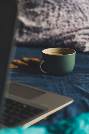 Tea with Lemon and Cookies with Chocolate Laying on Mattress - Grey Laptop Besides it, Blurred Turquoise Background, Vintage Look Editの写真素材