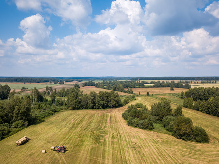 Aerial Drone Photo of Farmer Harvesting Hay Rolls in the Wheat Field with a Red Tractor - Sunny Summer Dayの写真素材