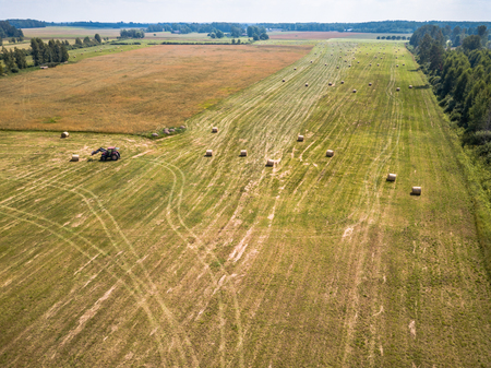 Aerial Drone Photo of Farmer Harvesting Hay Rolls in the Wheat Field with a Red Tractor - Sunny Summer Dayの写真素材