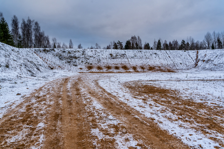 Car Tire Marks on an Empty Field Covered With Snow, Wood in the Backgroundの写真素材