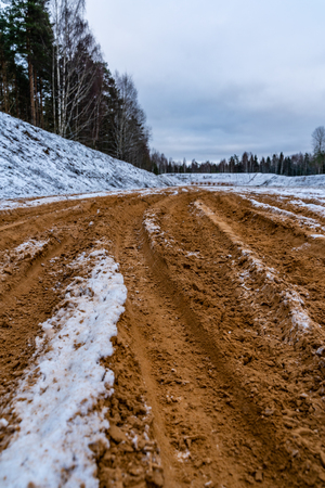 Car Tire Marks on an Empty Field Covered With Snow, Wood in the Backgroundの写真素材