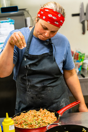 Female Chef Adding Salt to Salmon and Avocado Mix in Red Pan - Kitchen Setの写真素材