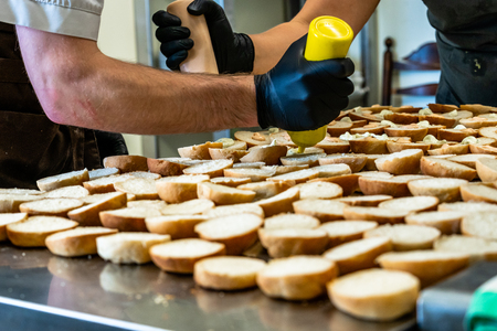 Male and Female Chef Spreading the Sauce on the Sliced Bread Spread on a Table for Small Burgers - Kitchen Setの写真素材