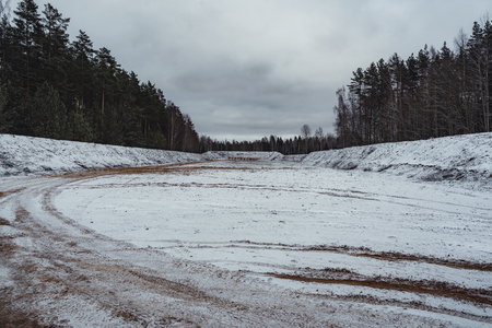 Car Tire Marks on an Empty Field Covered With Snow, Wood in the Background - Cloudy Day, Vintage Film Lookの写真素材
