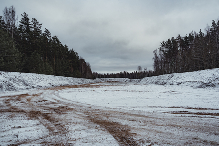 Car Tire Marks on an Empty Field Covered With Snow, Wood in the Background - Cloudy Day, Vintage Film Lookの写真素材