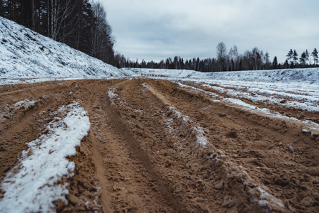 Car Tire Marks on an Empty Field Covered With Snow, Wood in the Background - Cloudy Day, Vintage Film Lookの写真素材