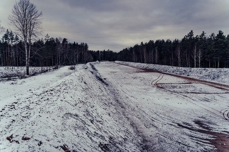 Car Tire Marks on an Empty Field Covered With Snow, Wood in the Background - Cloudy Day, Vintage Film Lookの写真素材