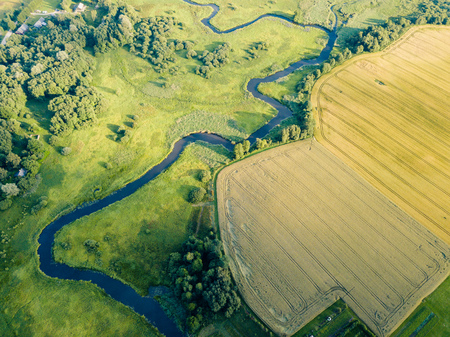 Aerial Photo the River Flowing Between Yellow and Green Agriculture Fields in Early Spring on Sunny Day - Concept of Peaceful Life in Countryside in Harmony and Traveling, Freedomの写真素材