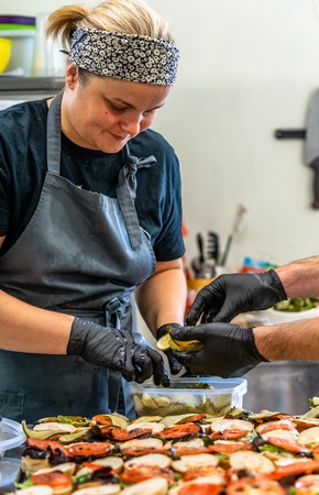 Female Chef Putting Ingredients of Burgers on a Sliced Bread Spread on a Table in Black Gloves - Concept of the Hard Working Person and the Hygiene in the Kitchenの写真素材