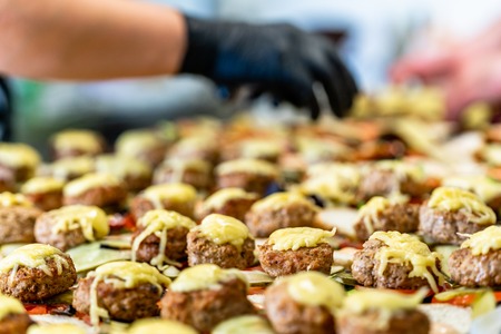 Female and Male Chef Putting Ingredients of Burgers on a Sliced Bread Spread on a Table in Black Gloves - Concept of the Hard Working Person and the Hygiene in the Kitchen, Partly Blurred Backgroundの写真素材