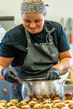 Female Chef Putting Ingredients of Burgers on a Sliced Bread Spread on a Table in Black Gloves - Concept of the Hard Working Person and the Hygiene in the Kitchen, Partly Blurred Foregroundの写真素材