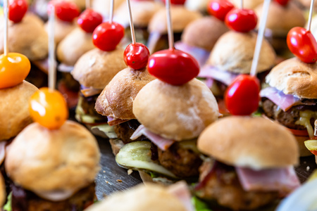 Closeup View of Small Handmade Burgers on the Table with Pickles, Tomatoes, Pork Cutlets and Salads as Ingredients - Kitchen Set, Concept of the Holiday Evening Dinner Tableの写真素材