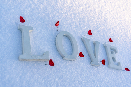 Closeup of Isolated Word "Love" from Wooden Pieces in the Snow on Sunny Winter Day with White Background with Red Heart Decorations Around it - Concept of Love, Happiness and Joy on Valentines Dayの写真素材