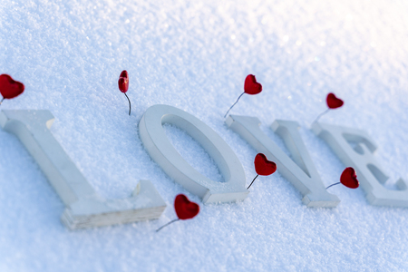 Closeup of Isolated Word "Love" from Wooden Pieces in the Snow on Sunny Winter Day with White Background with Red Heart Decorations Around it - Concept of Love, Happiness and Joy on Valentines Dayの写真素材
