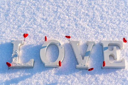 Closeup of Isolated Word "Love" from Wooden Pieces in the Snow on Sunny Winter Day with White Background with Red Heart Decorations Around it - Concept of Love, Happiness and Joy on Valentines Dayの写真素材