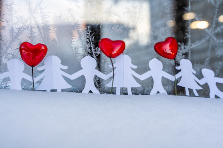 Isolated Chain of Origami Paper Boys and Girls Holding Hands With a Red Heart Between Them and the Hoarfrost on Window in Background - Concept of Love, Happiness and Joy on Valentines Dayの写真素材
