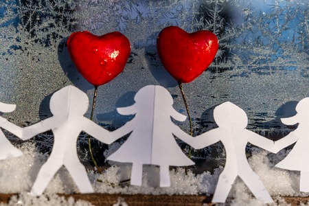 Isolated Chain of Origami Paper Boys and Girls Holding Hands With a Red Heart Between Them and the Hoarfrost on Window in Background - Concept of Love, Happiness and Joy on Valentines Dayの写真素材