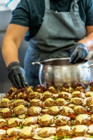 Female Chef Putting Ingredients of Burgers on a Sliced Bread Spread on a Table in Black Gloves - Concept of the Hard Working Person and the Hygiene in the Kitchen, Partly Blurred Foregroundの写真素材