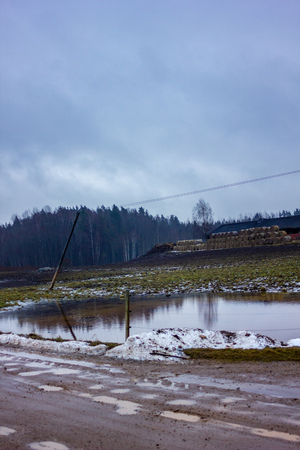 Empty Countryside Landscape in Cloudy Winter Day with Snow Partly Covering the Ground and Fog, Old Farm in the Background - Concept of Sadness and Lonelinessの写真素材
