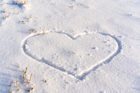 Closeup of the Heart Drawn in the Snow on the Ground on Sunny Winter Day - Concept of Love and Happinessの写真素材
