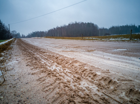 Empty Countryside Landscape in Cloudy Winter Day with Snow Partly Covering the Ground and Fog, Puddles and Tire Marks on the Road - Concept of Sadness and Lonelinessの写真素材